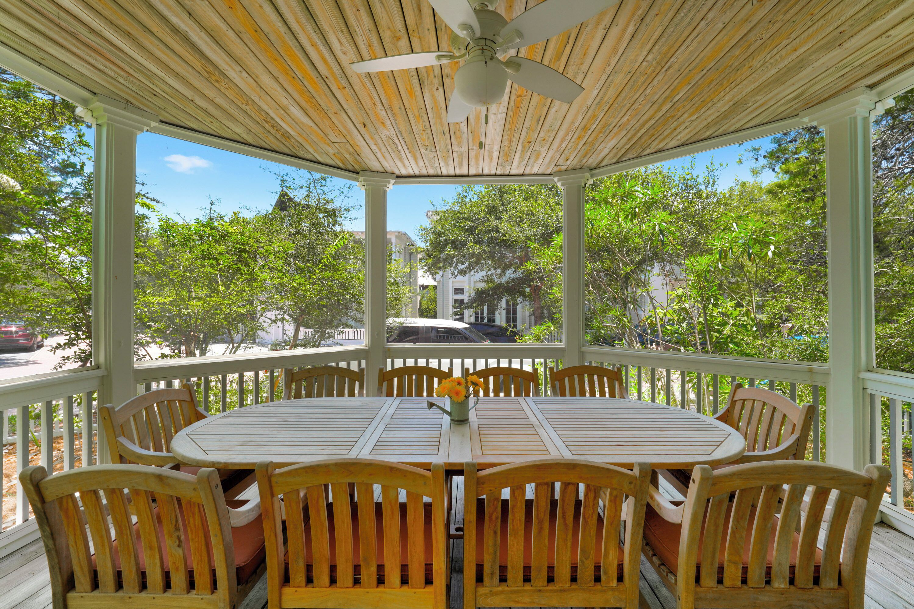 A covered outdoor seating area with a round table and wooden chairs, surrounded by a white railing.