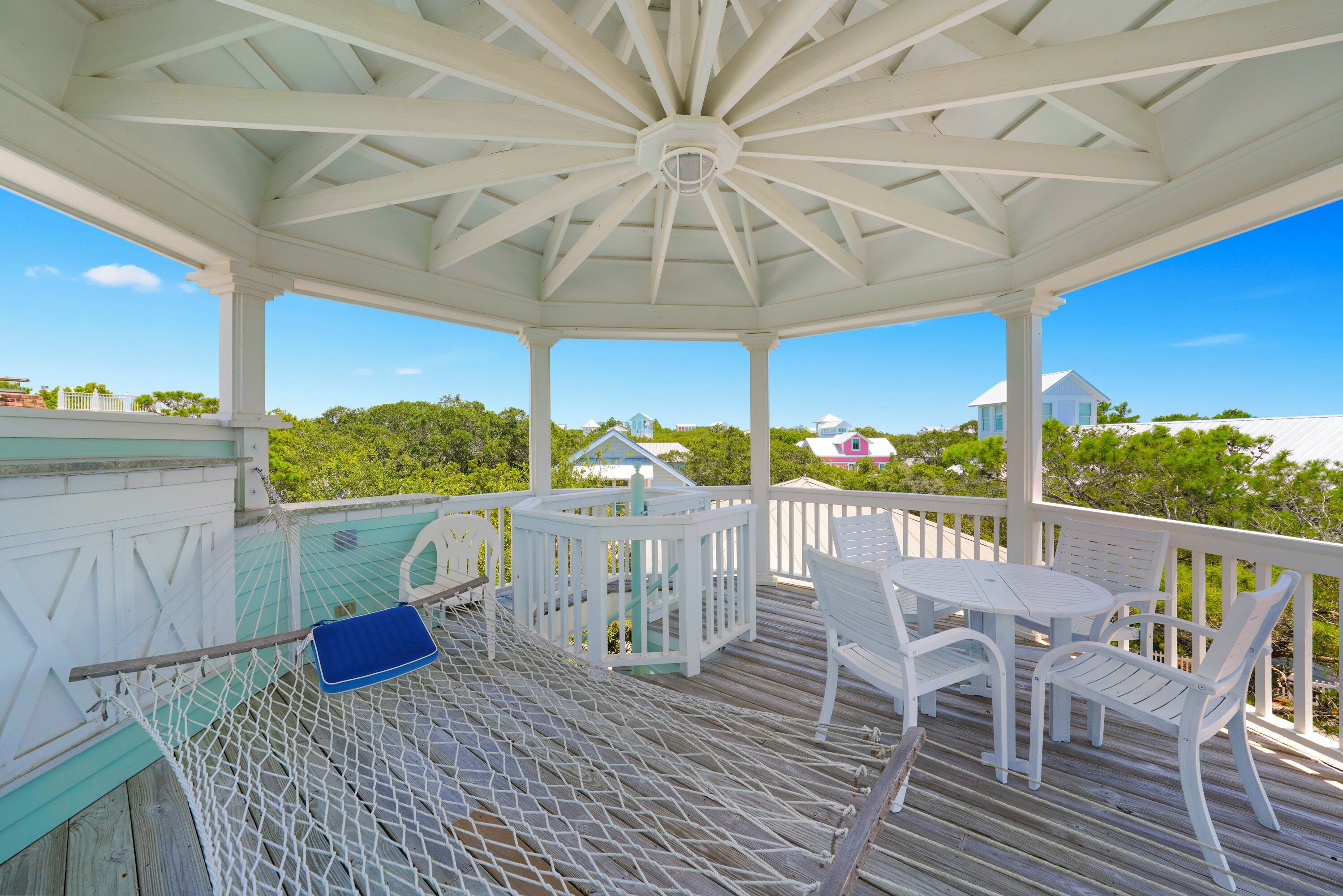 A covered outdoor area with a wooden deck, white furniture, and a hammock.