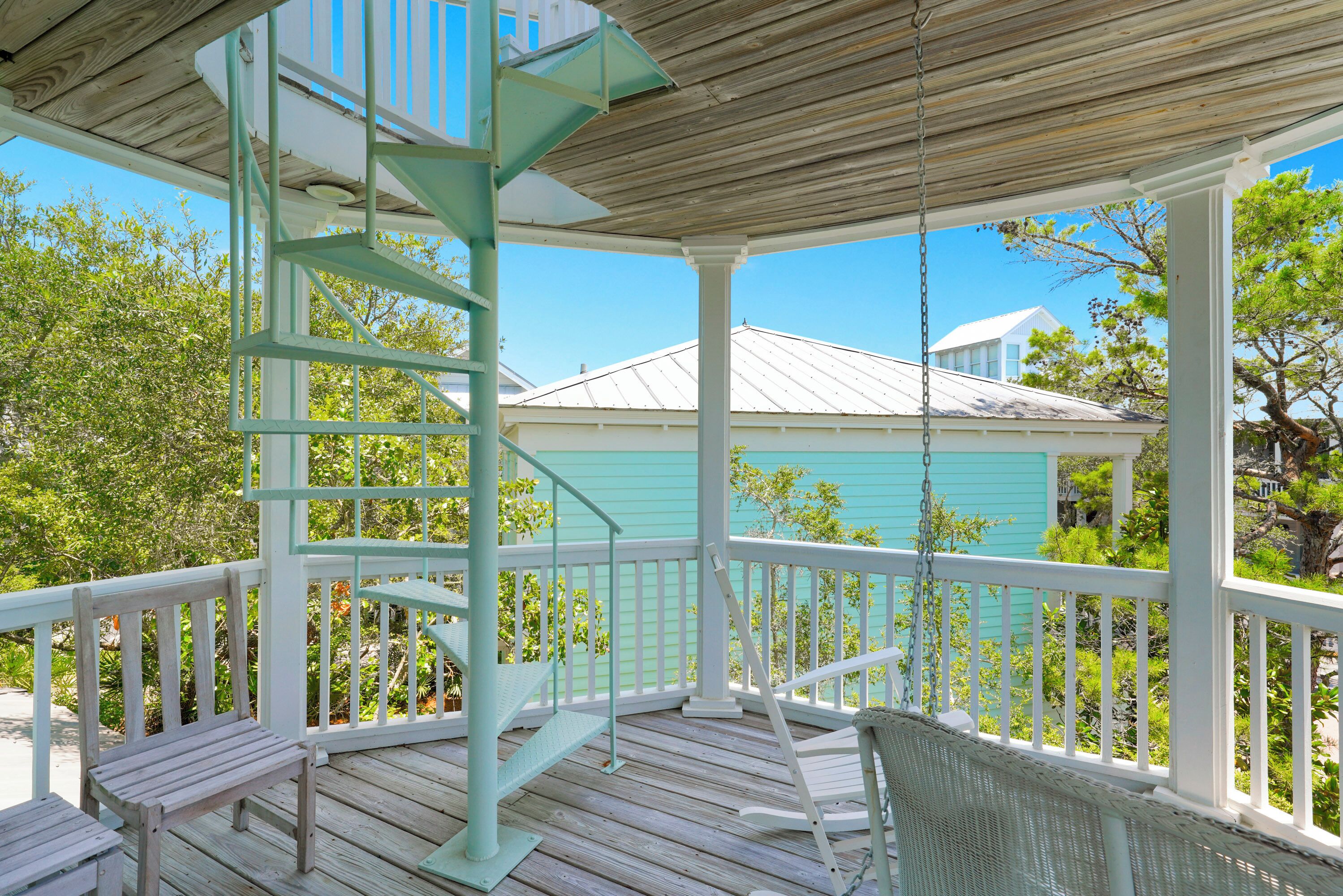 A wooden deck with a spiral staircase, white railings, and a view of a turquoise house.