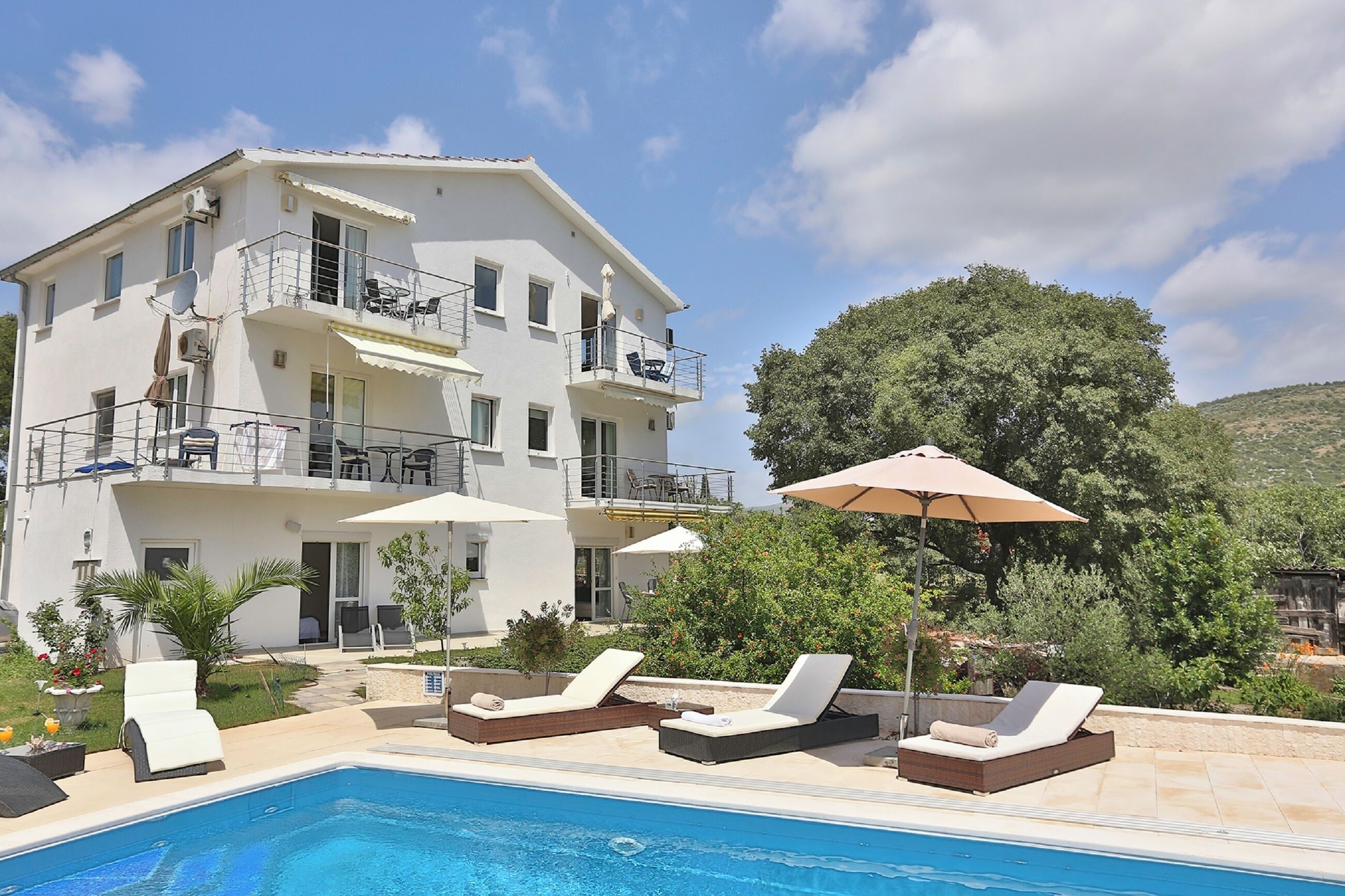 A multi-story building with a swimming pool, outdoor seating, and a view of a hill.