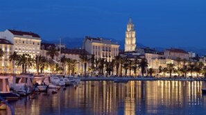 A waterfront cityscape with buildings, a prominent tower, and a marina with boats.