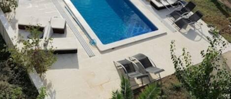 A rectangular swimming pool with a modern design, surrounded by lounge chairs and a covered area.