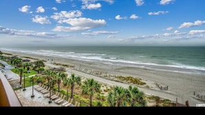 Blick auf einen Strand mit blauem Himmel, Palmen und einer Promenade mit Stühlen.