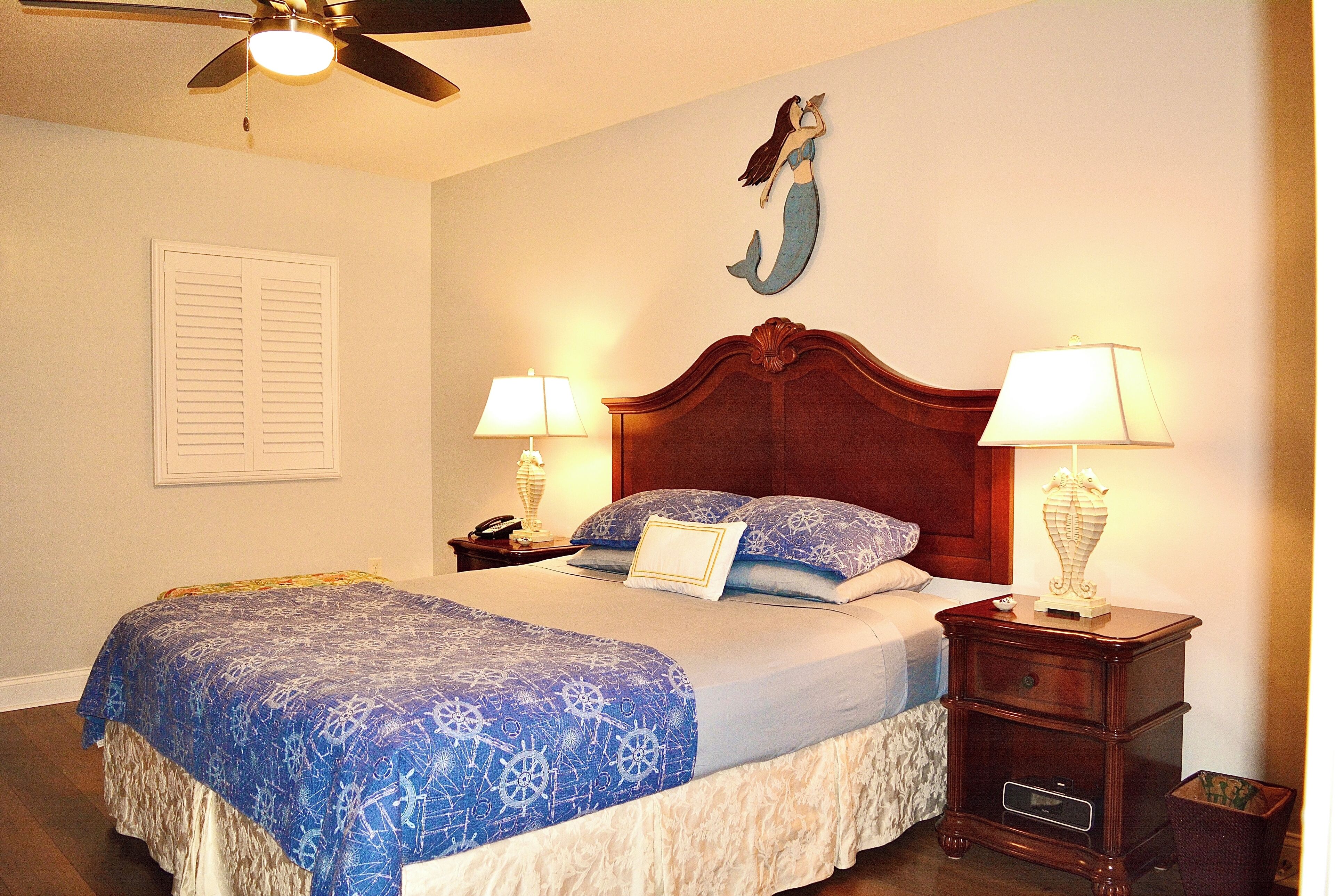 A neatly made bed with a blue and white patterned bedspread, two bedside lamps, a wooden nightstand, and a wall-mounted decorative piece.