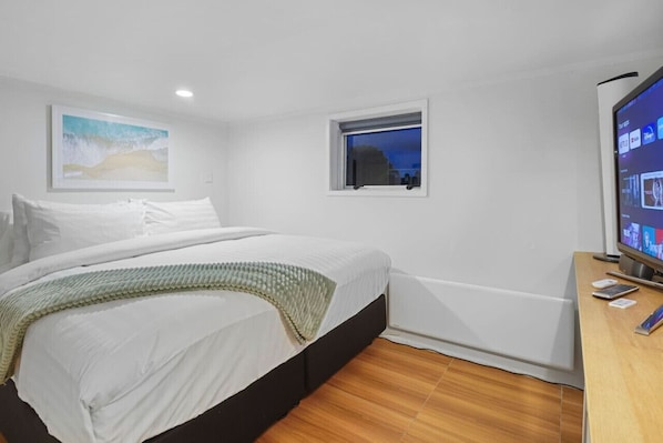 Een hotelkamer met een bed, een raam, een televisie en een houten vloer.