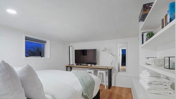 A modern bedroom with a bed, a desk, a television, and a bookshelf. - The Nifty Nook Studio with Parking and Wi-fi (Auckland West)