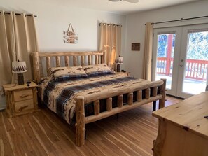 A wooden bed with a plaid bedspread in a room with wooden floors and a red balcony outside.