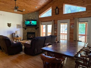 A cozy cabin interior with a stone fireplace, wooden furniture, and large windows.