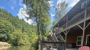 A lakeside deck with a fire pit, Adirondack chairs, and a deck with stairs leading to a building. - Riverfront Cabin w/ Porch & Firepit - Peaceful Retreat Near Murphy, NC. (Murphy)