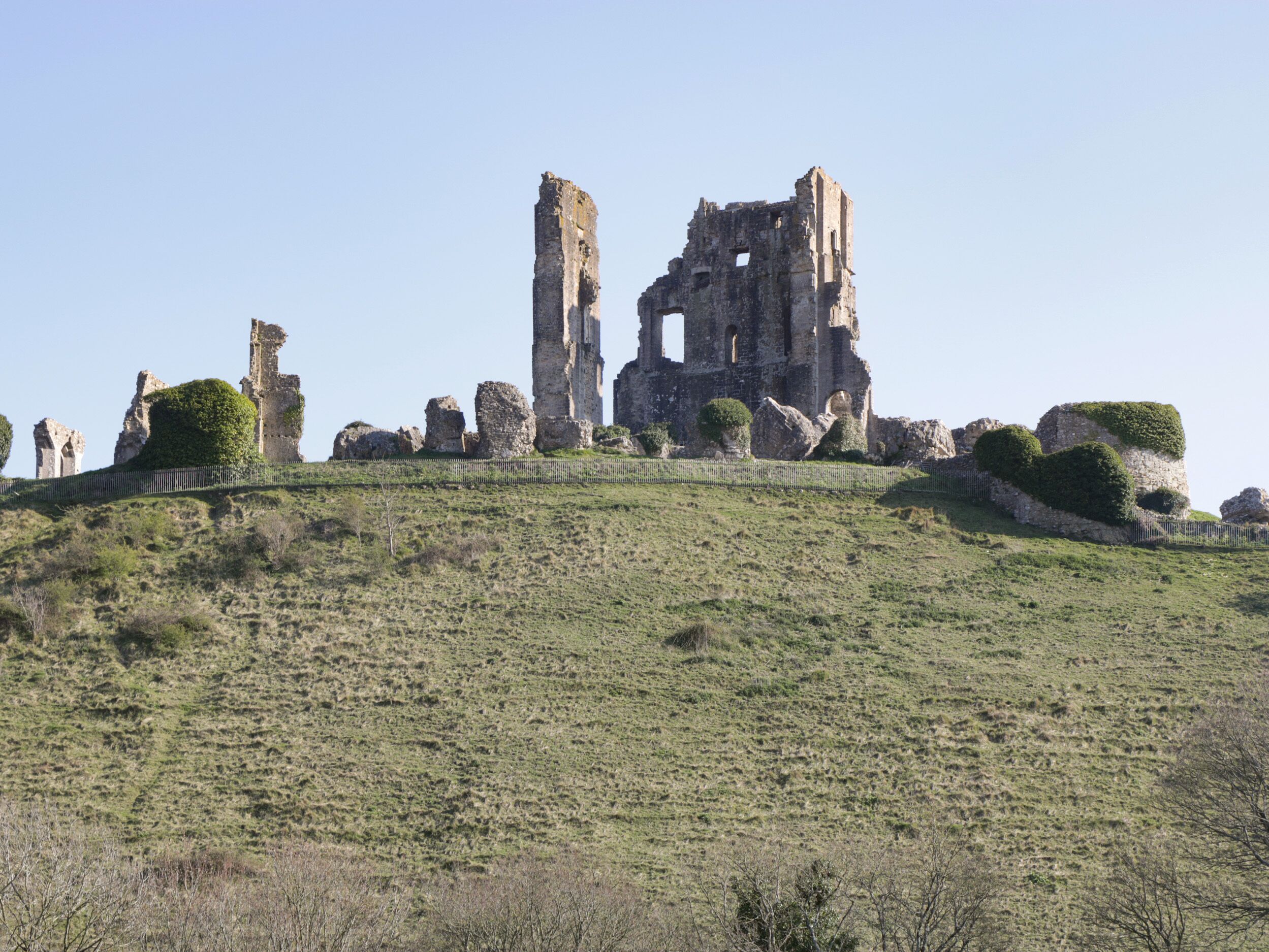 A historic stone ruin with multiple towers and walls, surrounded by a grassy hill.
