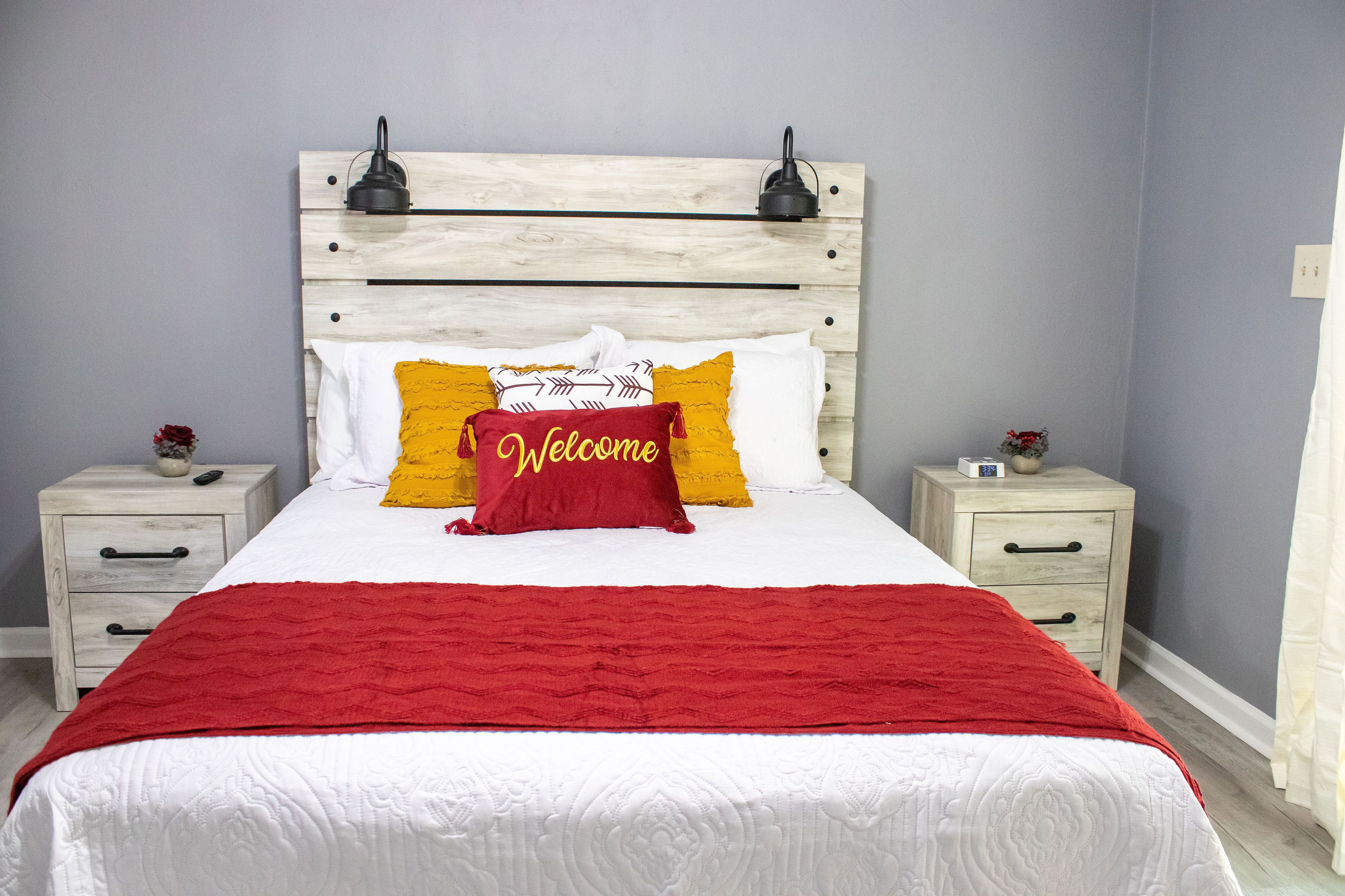 A neatly made bed with a red blanket, two bedside tables with lamps, and a headboard with a light wood finish.