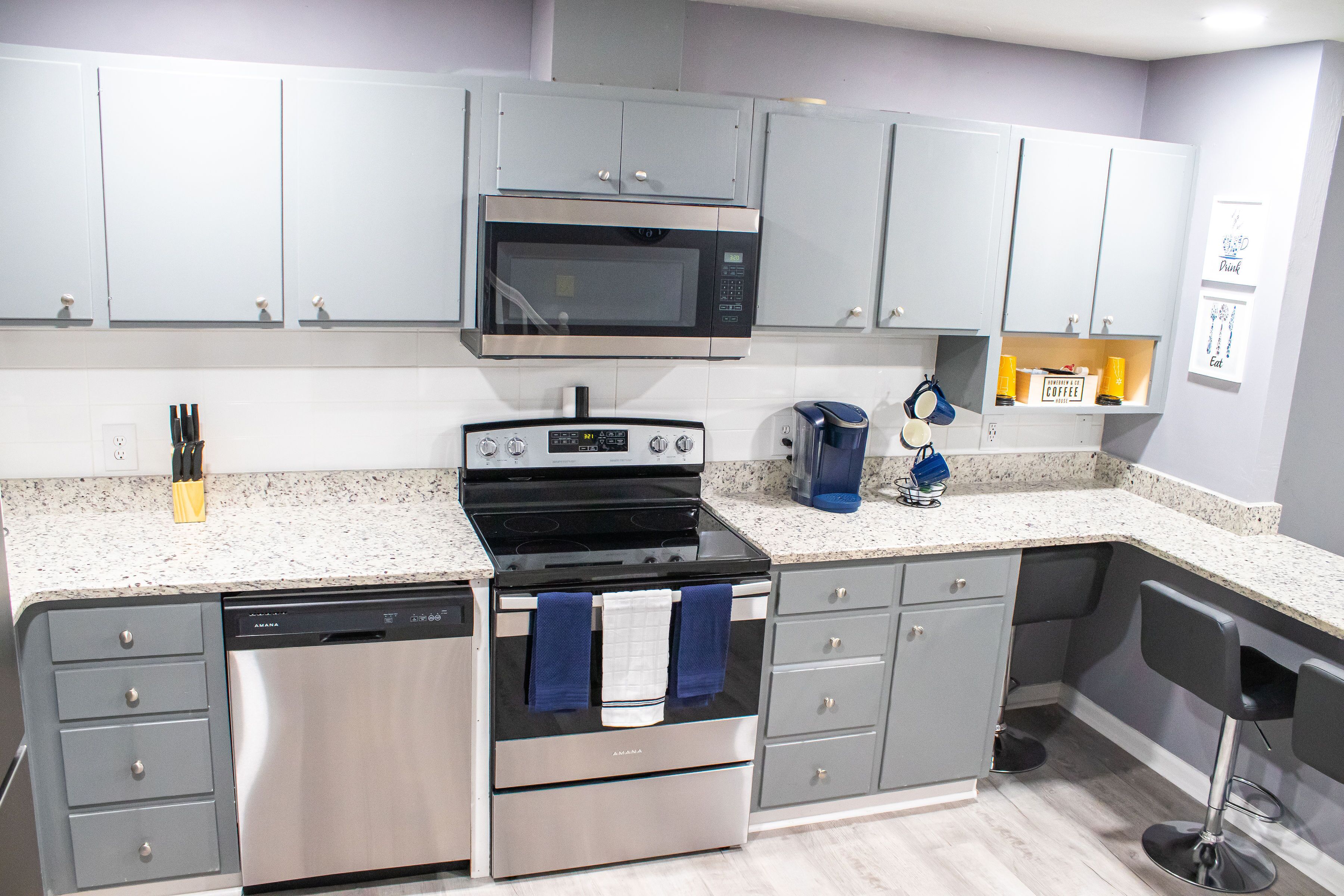 A modern kitchen with grey cabinets, a stainless steel dishwasher, an oven, and a microwave.