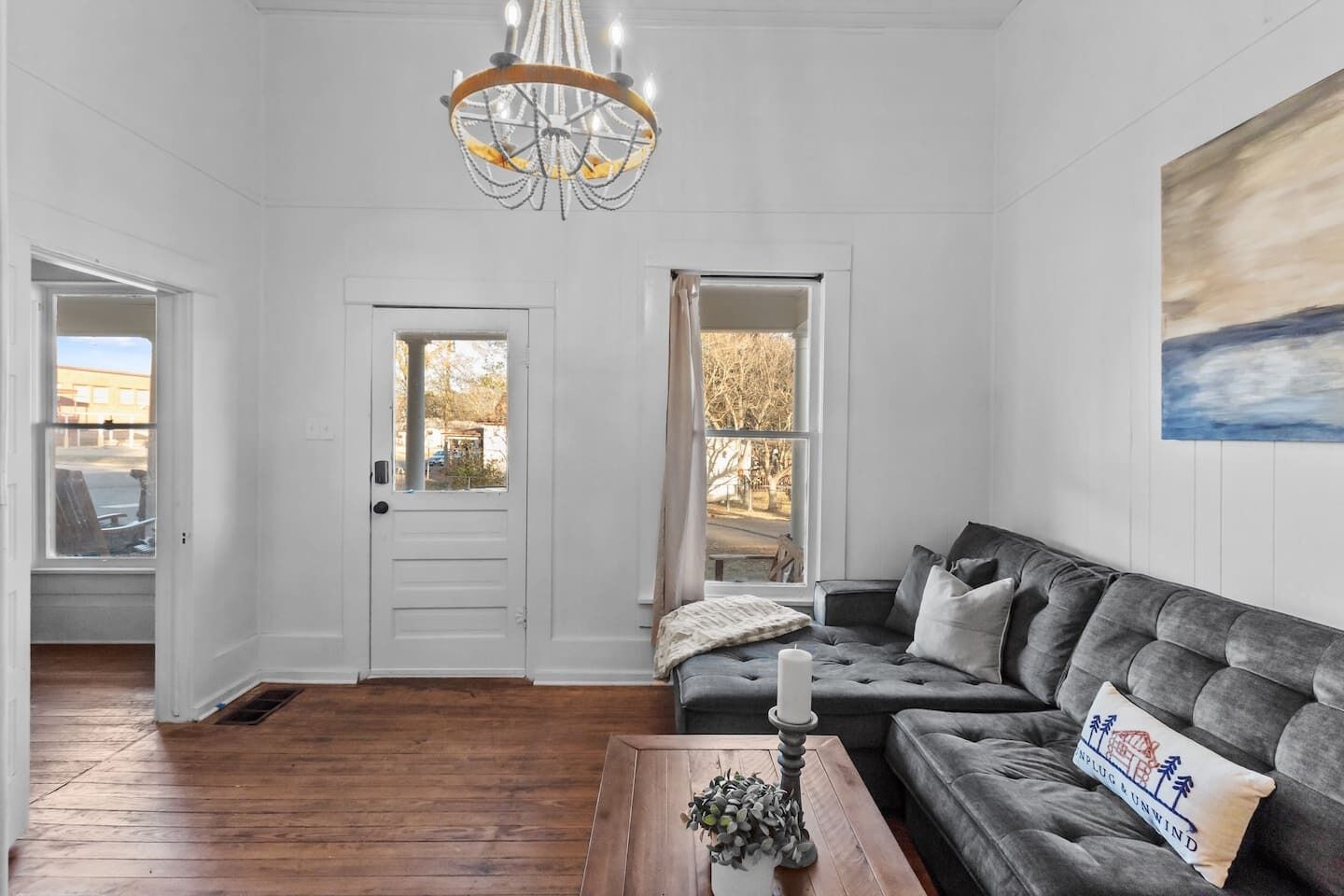 Un soggiorno con un divano grigio, un tavolino in legno, un lampadario e un quadro appeso al muro.
