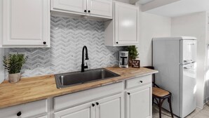 Eine moderne Küche mit weißen Schränken, einer Holz Arbeitsplatte, einem schwarzen Wasserhahn, einer Kaffeemaschine und einem weißen Kühlschrank.