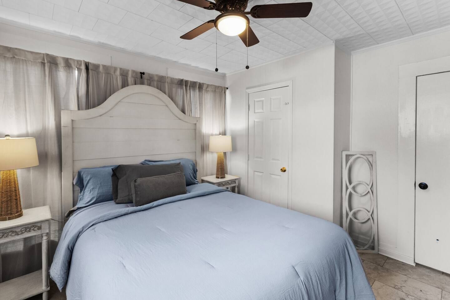 Una camera da letto con un letto, due comodini, una ventola a soffitto e una porta.