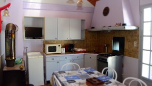 A compact kitchen with white cabinets, a microwave, a stove, and a sink. There is a dining table with chairs and a small decorative item on the table.