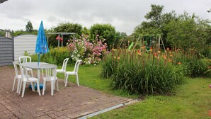 A patio with a table and chairs, surrounded by a garden with flowers and a swing set.