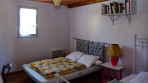 A bedroom with a bed, a bedside table with a lamp, a window, and a bookshelf.