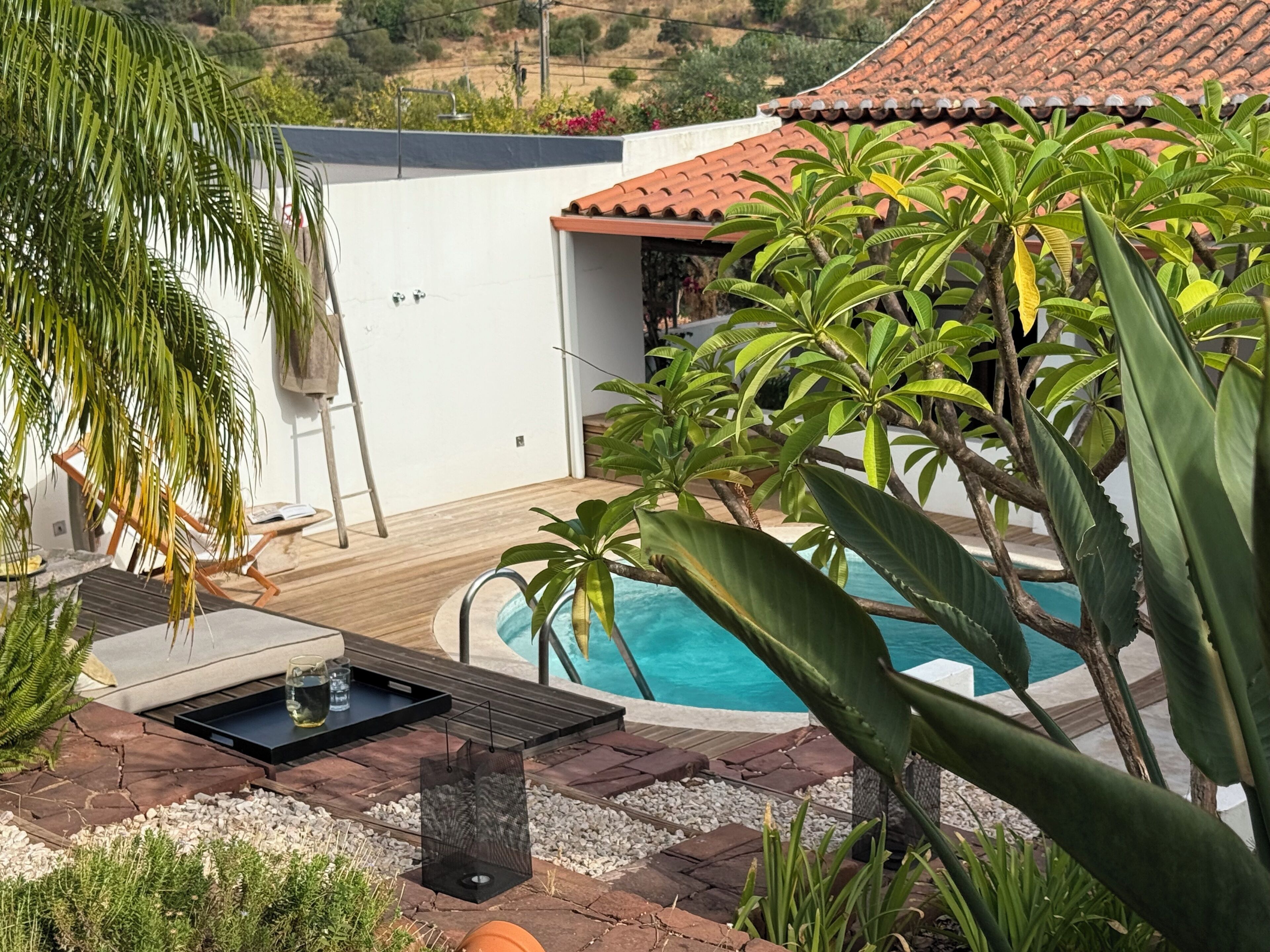A pool area with a wooden deck, a white wall, and a red-tiled roof.
