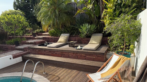 Eine Holzterrasse mit Pool, Liegestühlen und einer Leseecke mit Zeitschriften und Getränken.