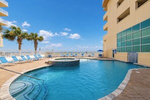 A swimming pool with lounge chairs and a hot tub, surrounded by a fence and palm trees. - BEACH FRONT 2BR at Crystal Shores West 807! (Gulf Shores)