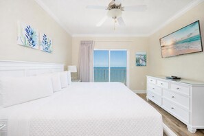 A hotel room with a large bed, a ceiling fan, a view of the ocean, and a white dresser. - BEACH FRONT 2BR at Crystal Shores West 807! (Gulf Shores)