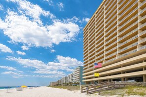 A beachfront hotel with multiple balconies, a sandy beach, and a clear sky.