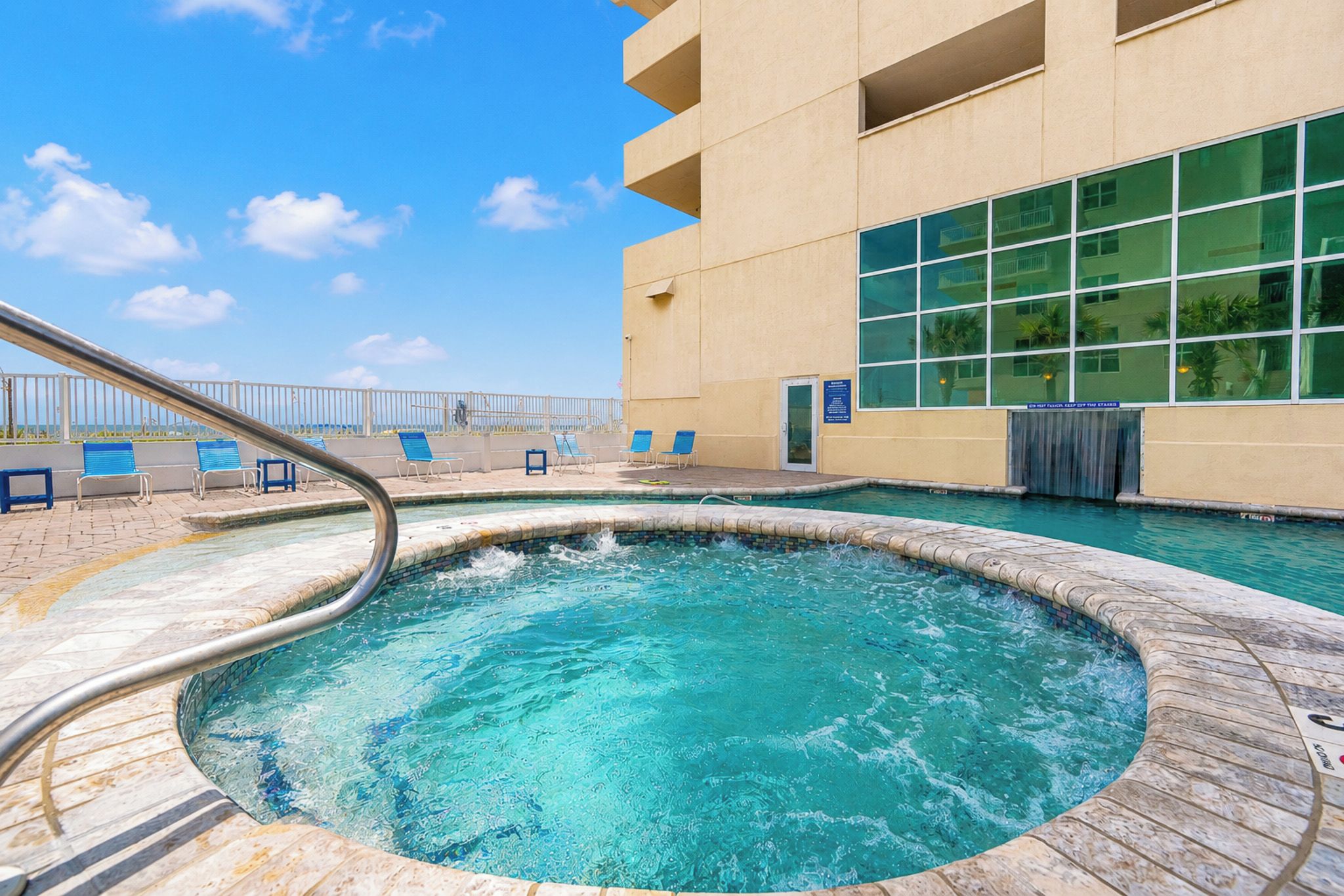 A swimming pool with a metal ladder, surrounded by lounge chairs and a building with large windows.