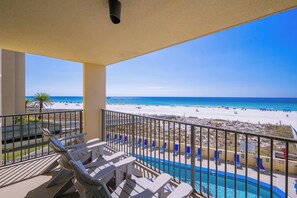 A balcony with chairs overlooking a pool and beach.
