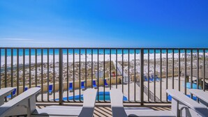Un balcón con vista a la playa, sillones de descanso y una zona de piscina.