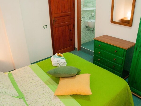 A bedroom with a green bedspread, a wooden door, a green dresser, and a bathroom visible through an open door.