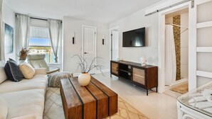 En moderne stue med sofa, sofabord, fjernsyn og en skydedør til et badeværelse.