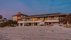En ejendom ved stranden med en flersidet bygning, herunder en balkon og en trappe til indgangen.