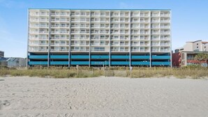 A multi-story hotel with a blue and white facade, located on a sandy beach.