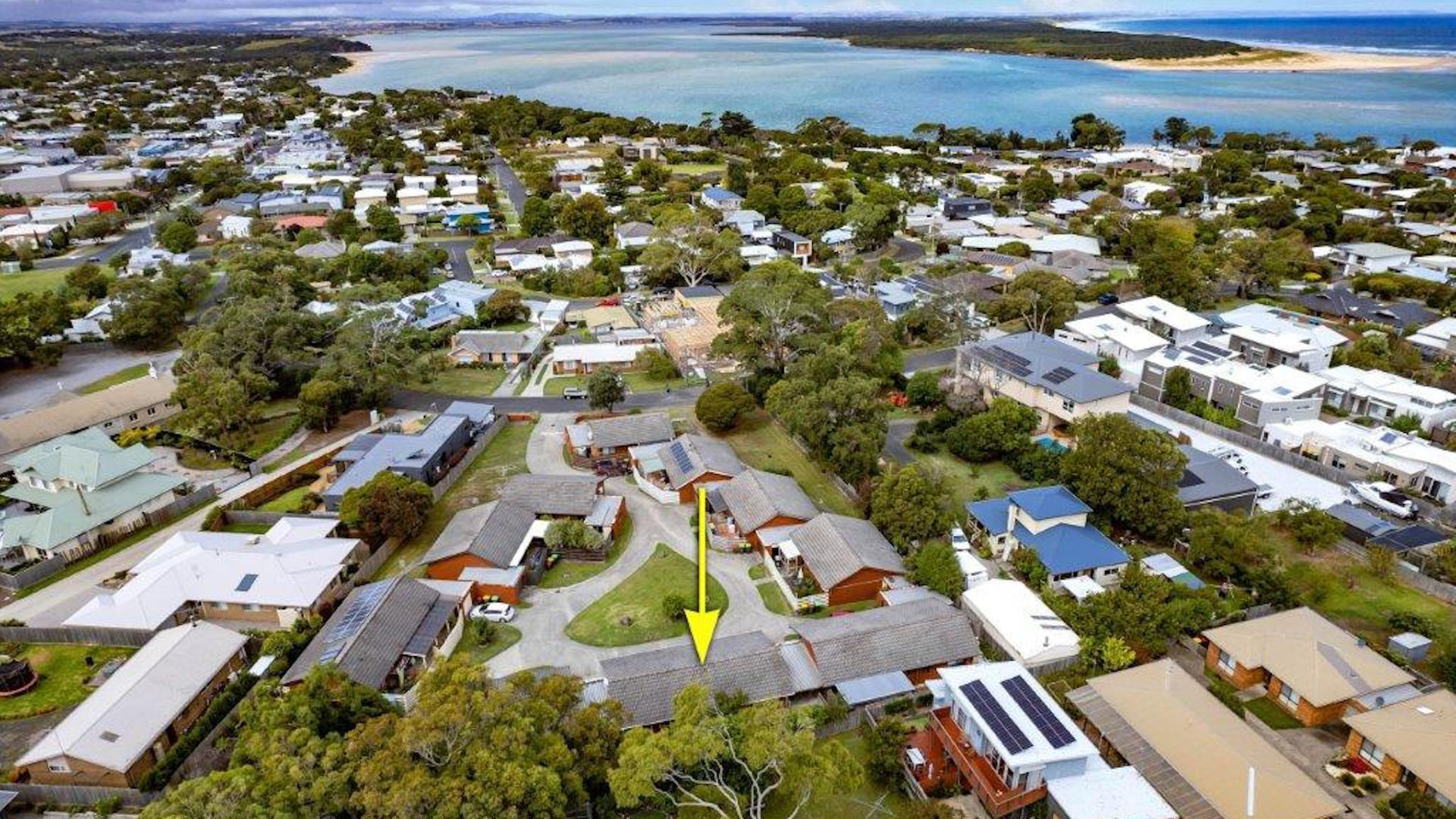 An aerial view of a residential area with houses, green spaces, and a beach in the background.