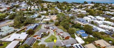 An aerial view of a residential area with houses, green spaces, and a beach in the background.