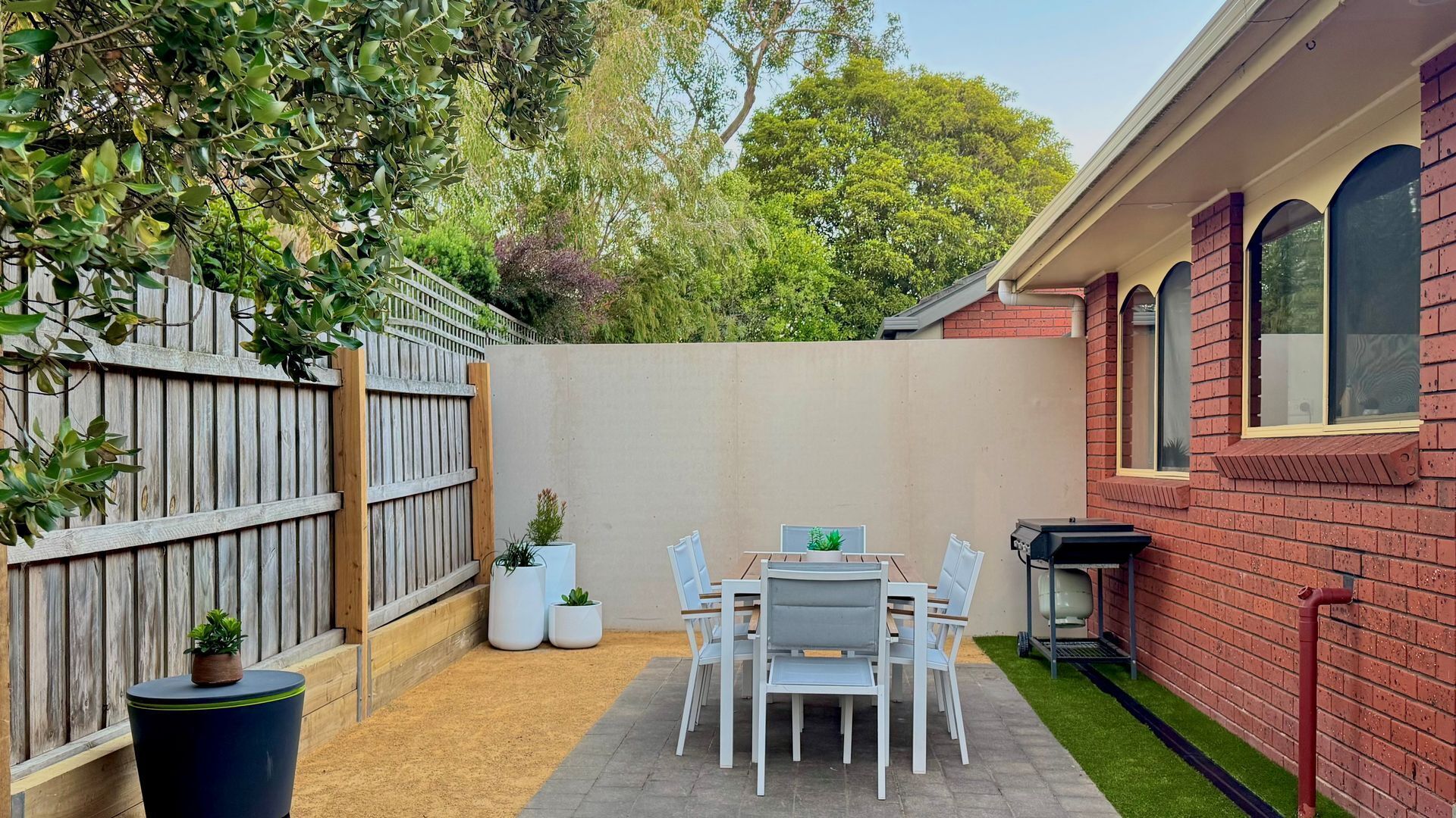 Une terrasse avec une table et des chaises, entourée d  ’une clôture en bois et d’un mur en briques.