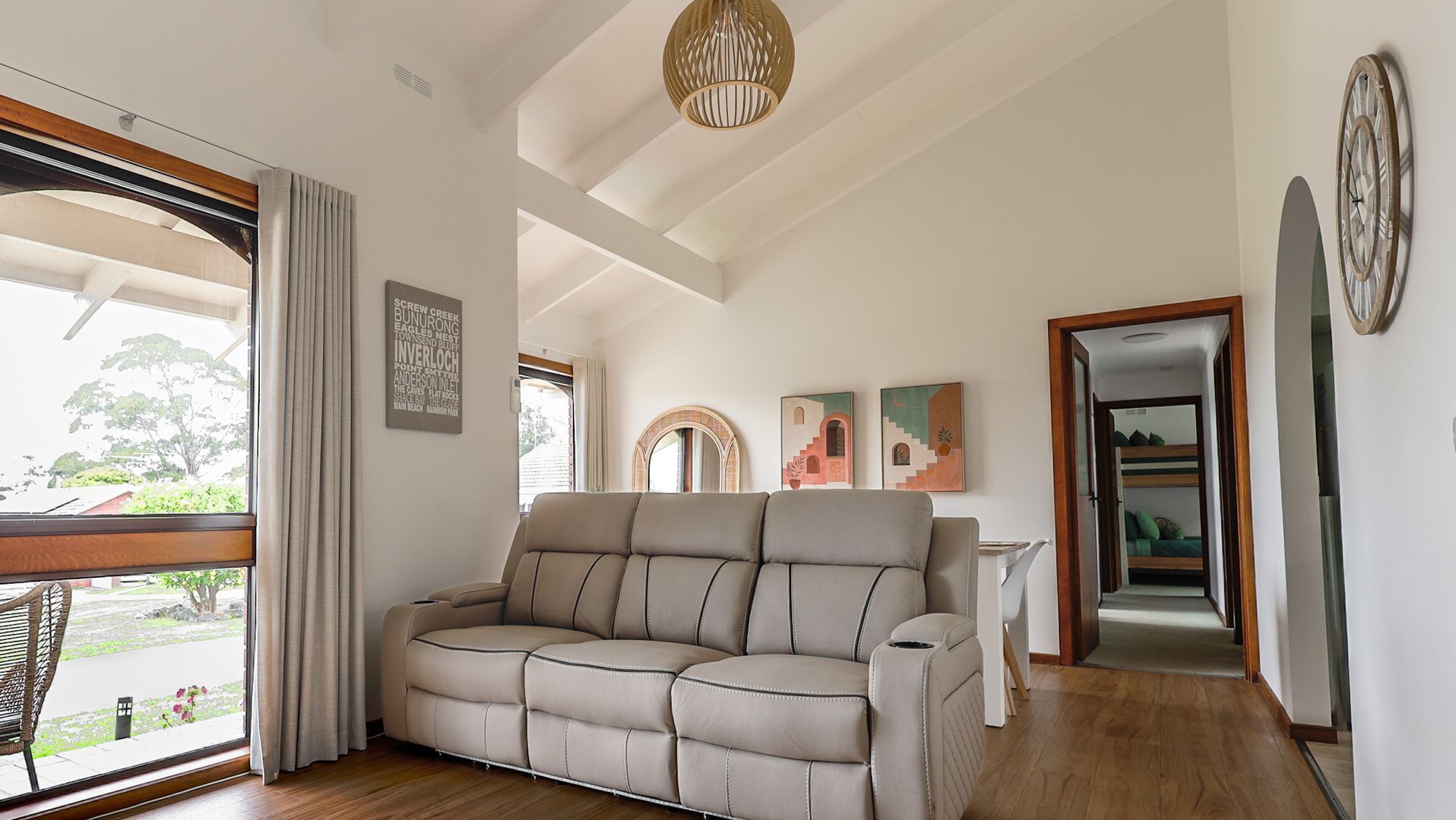 A modern living room with a beige sofa, a wooden-framed mirror, and a ceiling light fixture.