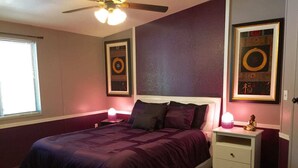 Ein Schlafzimmer mit einem Bett, zwei Nachttischen, einem Deckenventilator und zwei gerahmten Kunstwerken an den Wänden.
