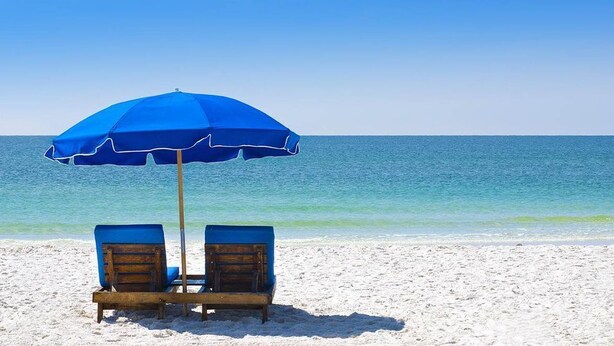 Una playa con dos sillones de madera bajo una sombrilla azul.