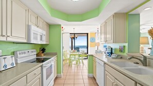 Una cocina con electrodomésticos blancos, paredes verdes y vista al océano a través de una puerta.