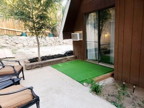 Un patio con posti a sedere all'aperto, una piccola area verde in prato e un edificio in legno con una porta in vetro.