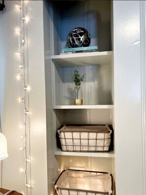 Un mur blanc orné d’une guirlande lumineuse, une étagère avec un casque, une petite plante et deux paniers en fil de fer.