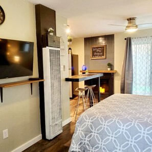 Una habitación de hotel con cama, televisión, kitchenette y ventilador de techo.