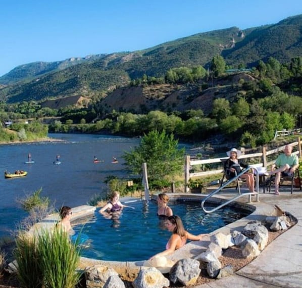 Ein Poolbereich mit entspannten Menschen, umgeben von Naturlandschaft und Blick auf das Wasser.