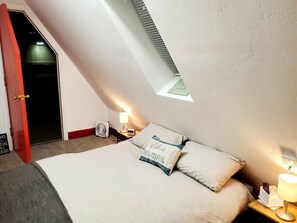 An attic bedroom with a sloped ceiling, a bed with pillows, a nightstand with a lamp, and a fan. - Cabin 17: Cozy 2-Story Retreat w/ Spiral Staircase • Kitchen • Sleeps 4 (Glenwood Springs)
