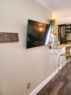 Una cocina moderna con una televisión de pantalla plana montada en la pared, una pequeña barra y una escalera que sube a un nivel superior.