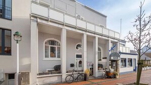 A white building with a covered porch, large windows, and a bicycle parked outside. - Starfish, city center, central location, wifi, very quiet (Norderney)