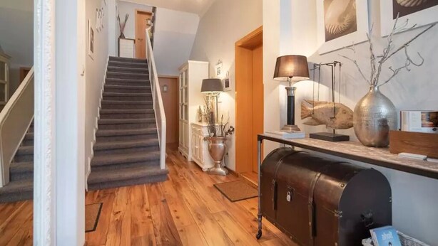 A hallway with a wooden floor, a staircase, a white cabinet, a lamp, and a decorative vase. - Starfish, city center, central location, wifi, very quiet (Norderney)