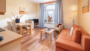 A modern living room with a wooden dining table, a sofa, and a TV. - Starfish, city center, central location, wifi, very quiet (Norderney)